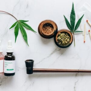 Top view of cannabis products including CBD oils, leaves, and smoking accessories on a marble surface.