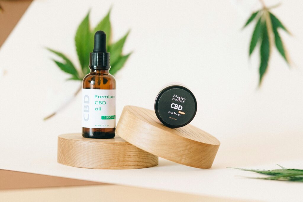 A premium CBD oil and pain relief salve set on wooden pedestals with a hemp leaf in the background.